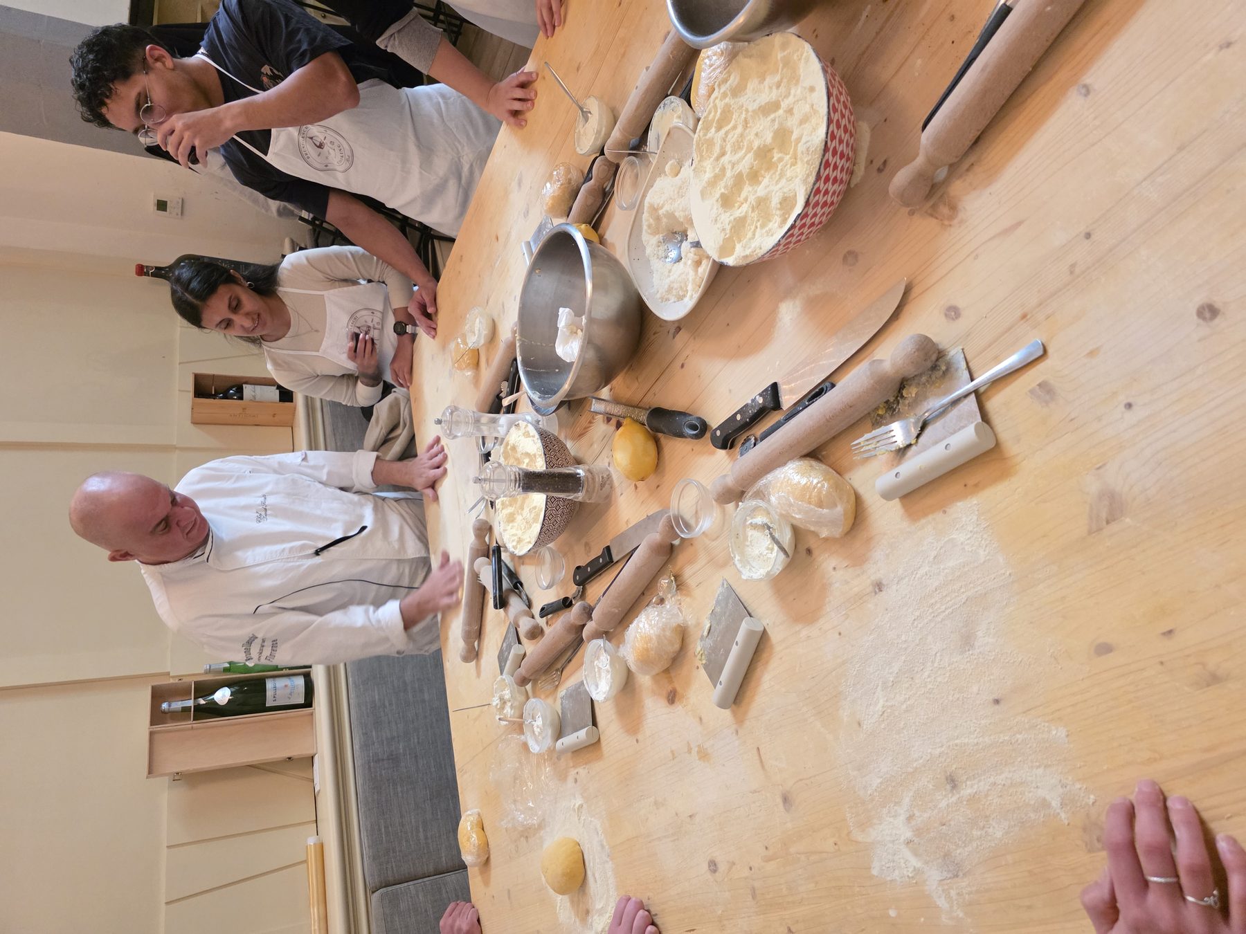 A chef in whites with students around a long wooden table, dough and rolling pins, Florence