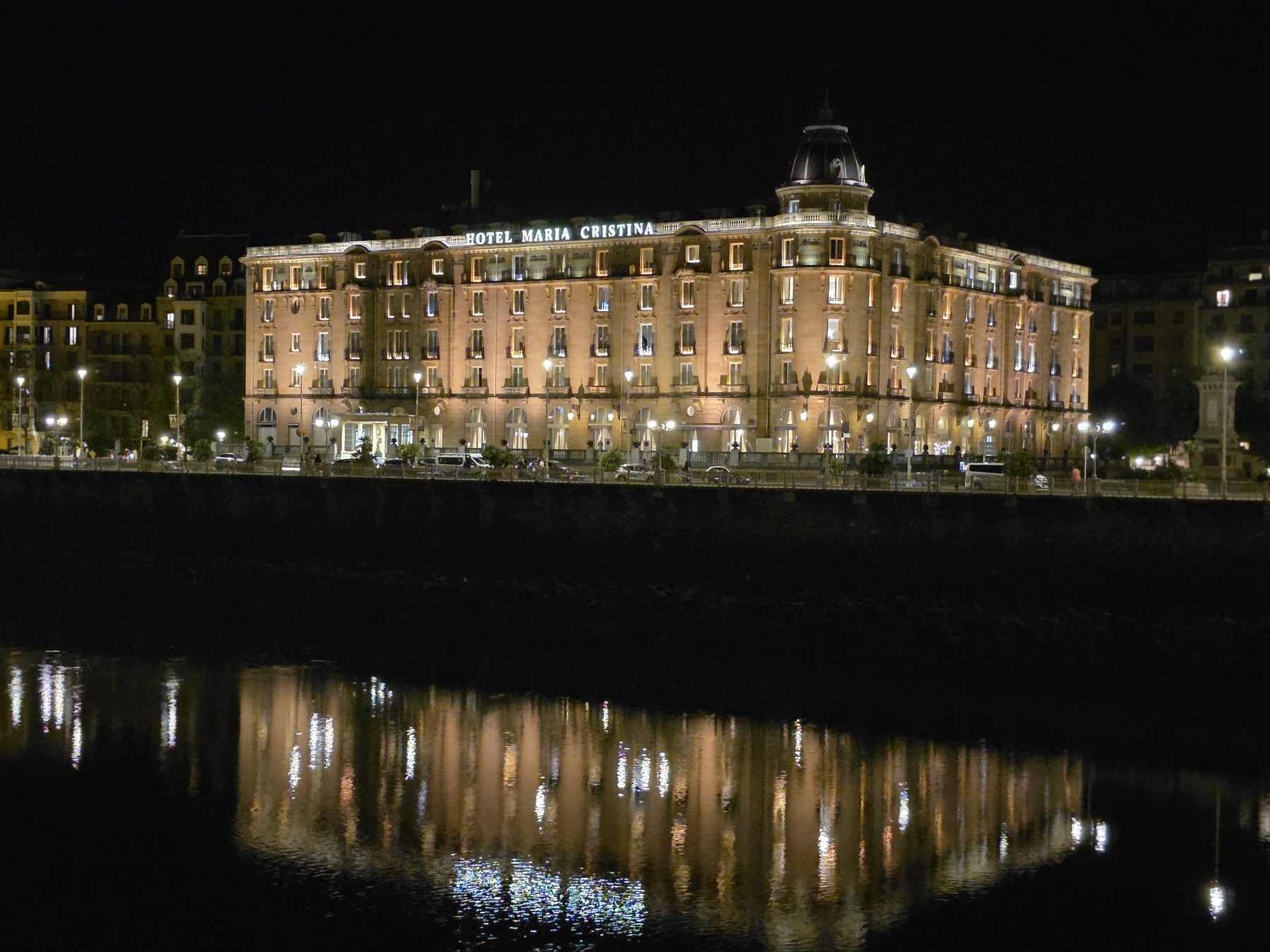 The Hotel María Cristina in San Sebastián lit at night, reflected on the Urumea river